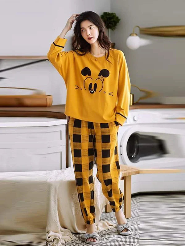 Woman wearing a yellow pajama set with cartoon face design in a room.