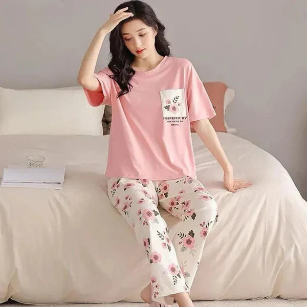 Woman wearing a pink pajama top and floral pants sitting on a bed.