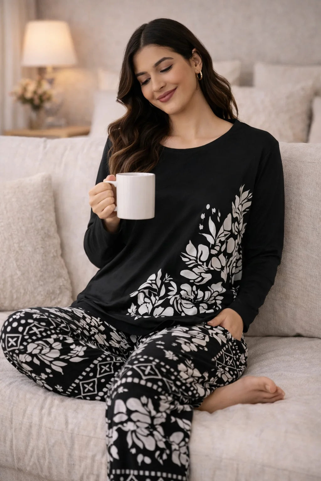 Woman in black and white patterned pajamas holding a mug on a couch.