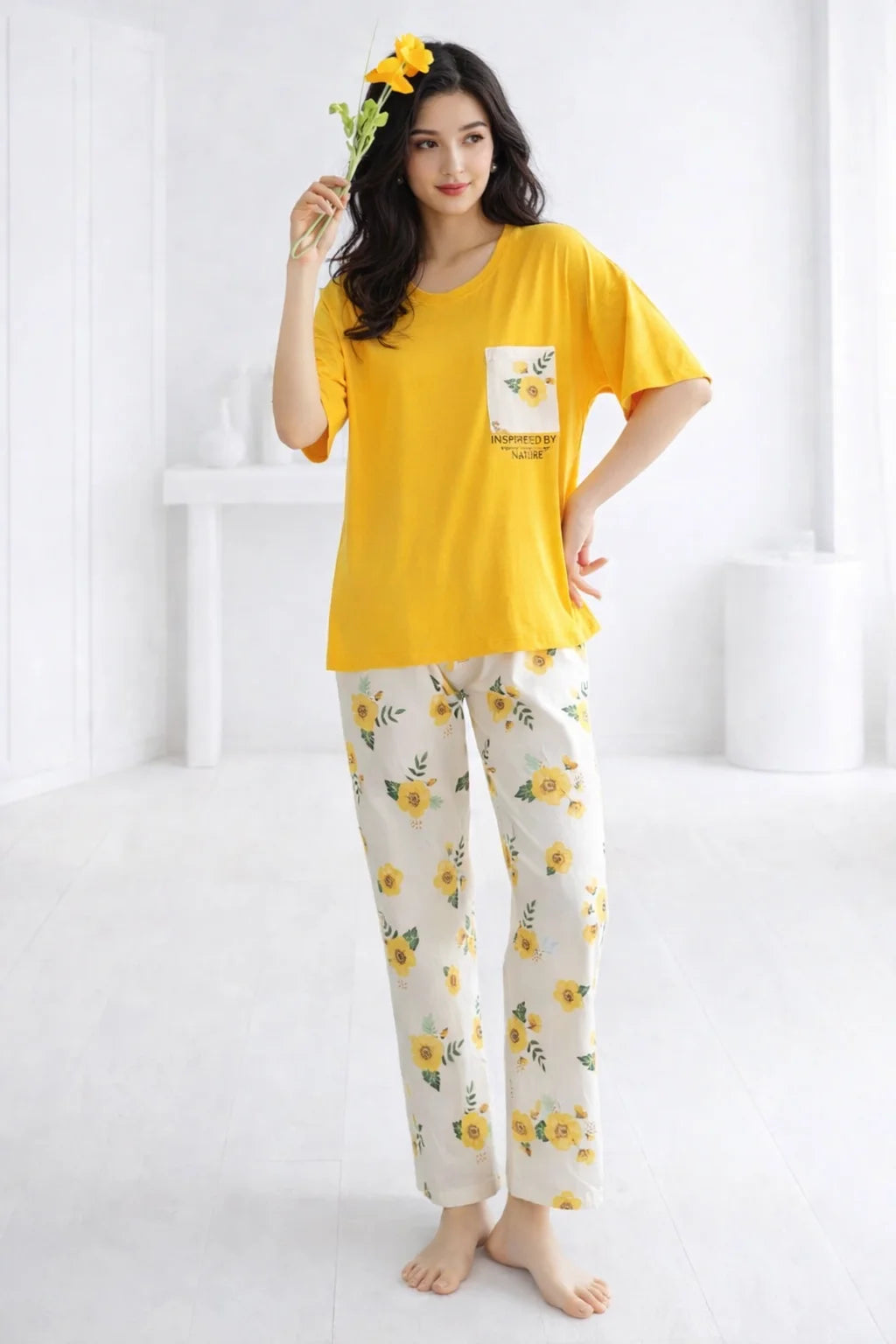 Woman wearing a yellow top and floral pants holding a flower, on a white background