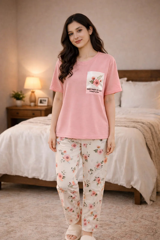 Woman wearing a pink pajama top with a floral design and matching pants in a bedroom setting.