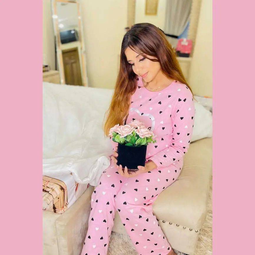 Woman in pink pajamas with black heart patterns sitting on a couch holding a small plant.
