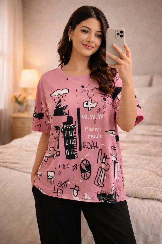 Woman taking a mirror selfie wearing a pink t-shirt with black graphics in a bedroom setting.