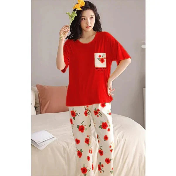 Woman wearing a red top and floral pants, holding flowers in a bedroom setting.
