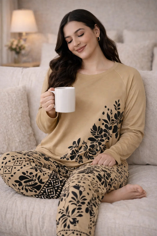 Woman in beige pajama set with black patterns sitting on a couch holding a white mug.