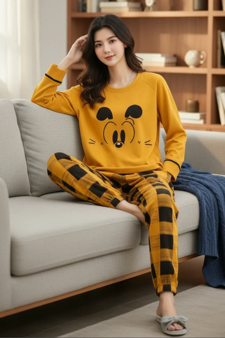 Woman wearing a yellow pajama set with a cartoon face design, sitting on a couch.