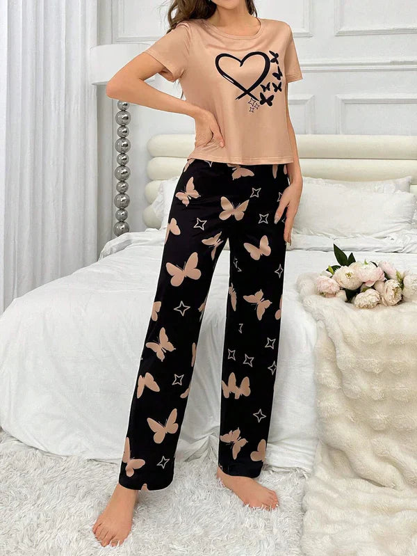 Woman wearing a beige t-shirt and black pants with butterfly patterns in a bedroom setting.