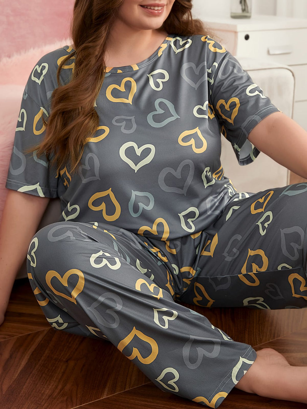 Woman wearing a gray pajama set with colorful heart patterns sitting on a bed.