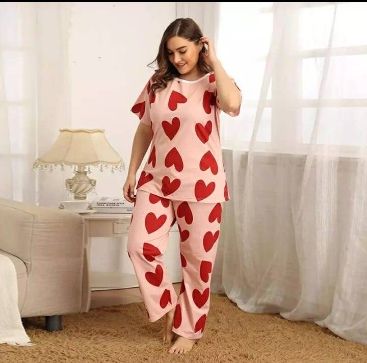 Woman wearing a pink pajama set with red heart patterns in a room.